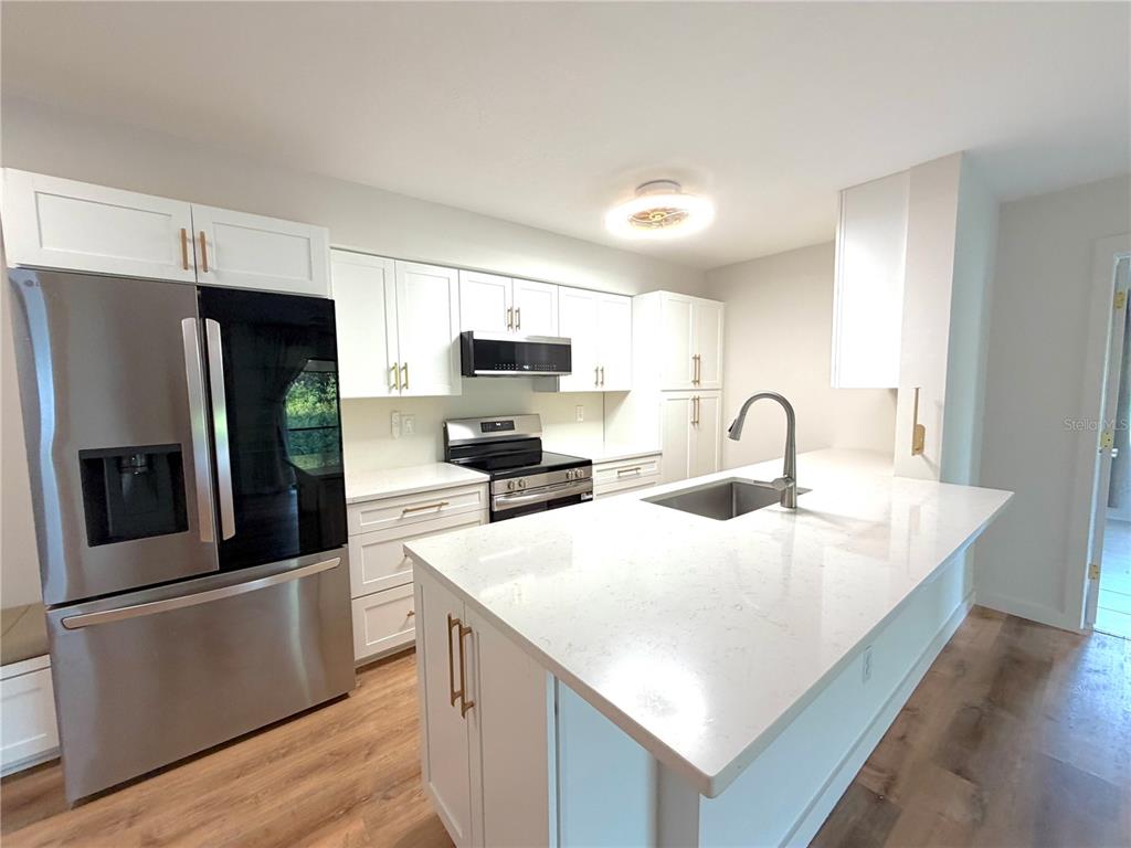 A modern kitchen features white cabinetry, stainless steel appliances, and a large quartz-topped island — 2067 HUNTERS GLEN DRIVE UNIT 312, DUNEDIN, FL