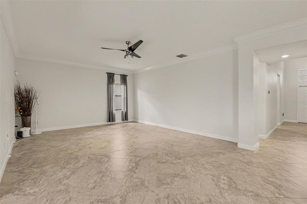 An empty living room features light-colored tile flooring, white walls, and a ceiling fan — 12005 CINNAMON FERN DRIVE, RIVERVIEW, FL