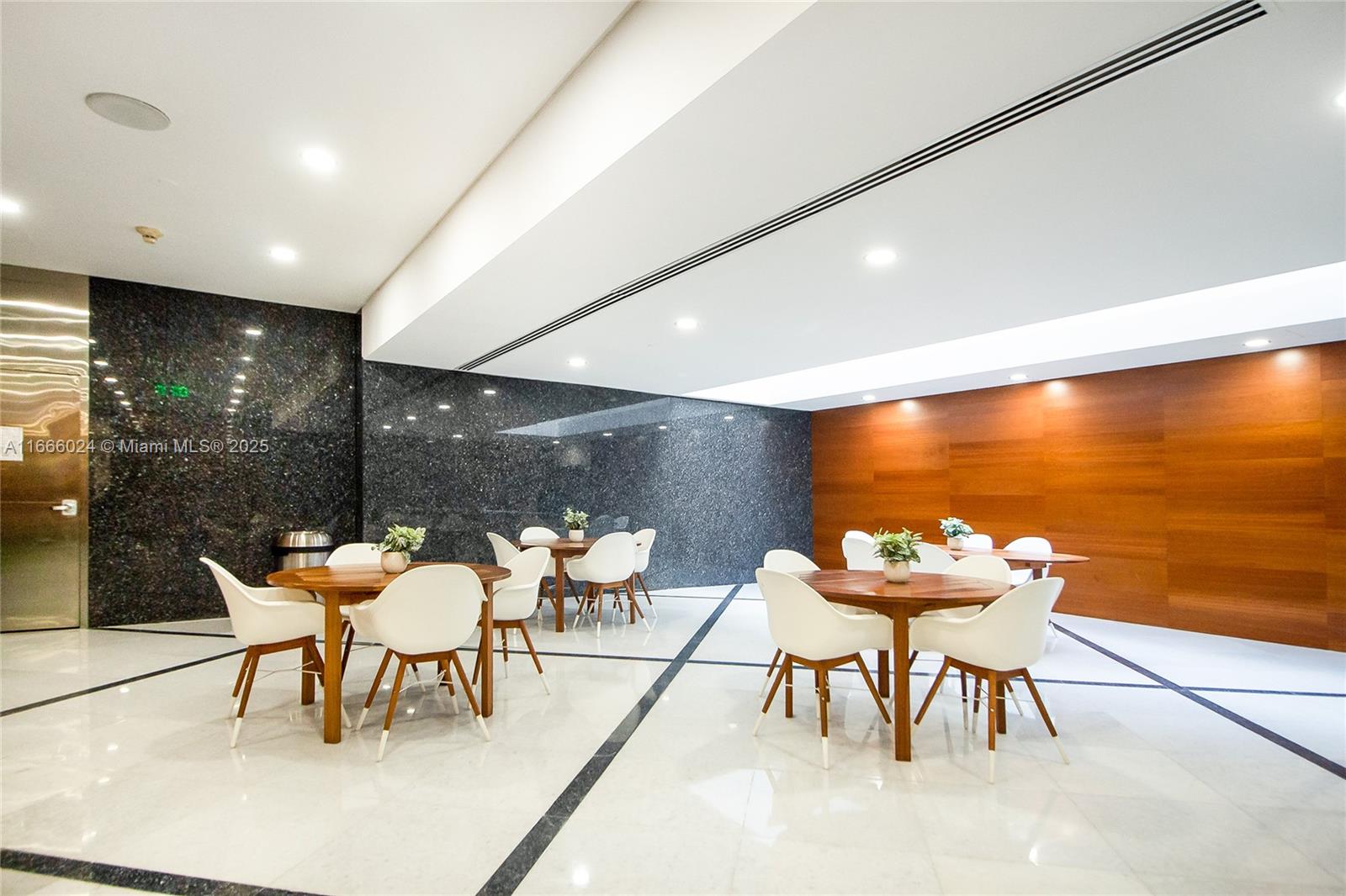 A modern lobby features white tile floors, dark granite walls, wood paneling, and circular dining sets — 1200 Brickell Ave # D, Miami FL 33131, MIAMI, FL