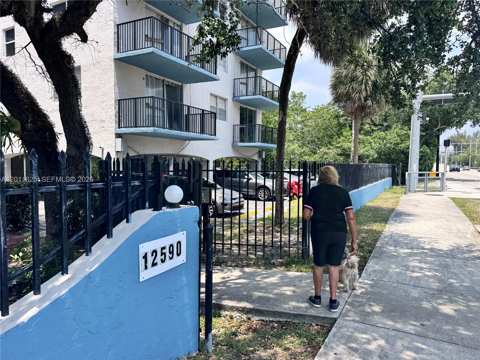 A woman walks a small dog on a sidewalk beside a multi-story apartment building — 12590 NE 16th Ave # 209, North Miami FL 33161, NORTH MIAMI, FL