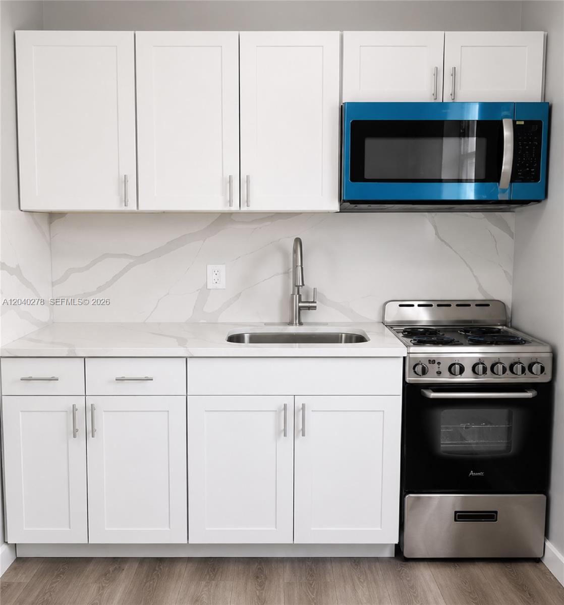 A small kitchen features white cabinets, a marble-patterned backsplash, a stainless steel stove, and a microwave — 1801 NW 54th St, Miami FL 33142, MIAMI, FL