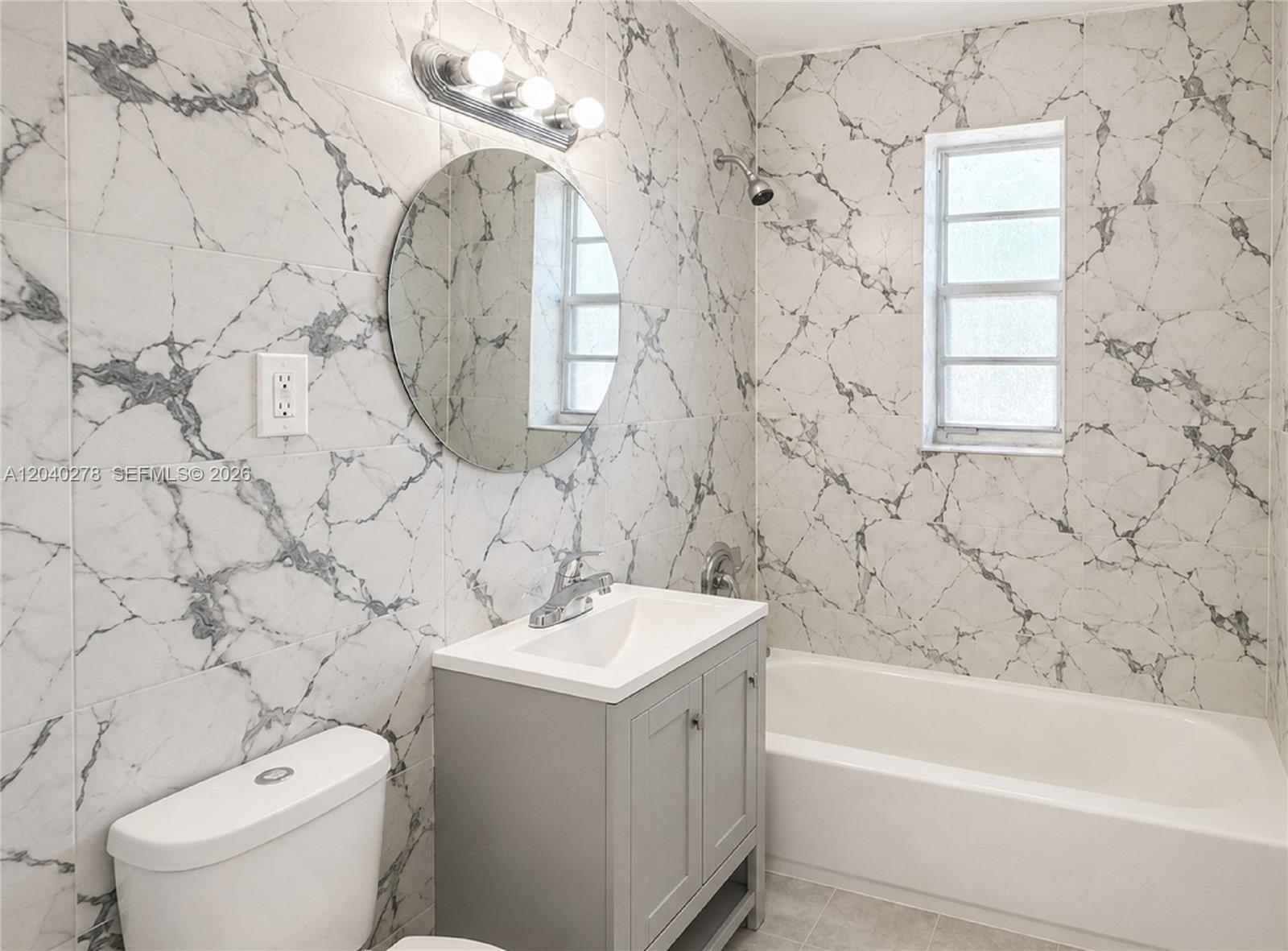 A bathroom features marble-patterned wall tiles, a gray vanity, a round mirror, and a bathtub — 1801 NW 54th St, Miami FL 33142, MIAMI, FL
