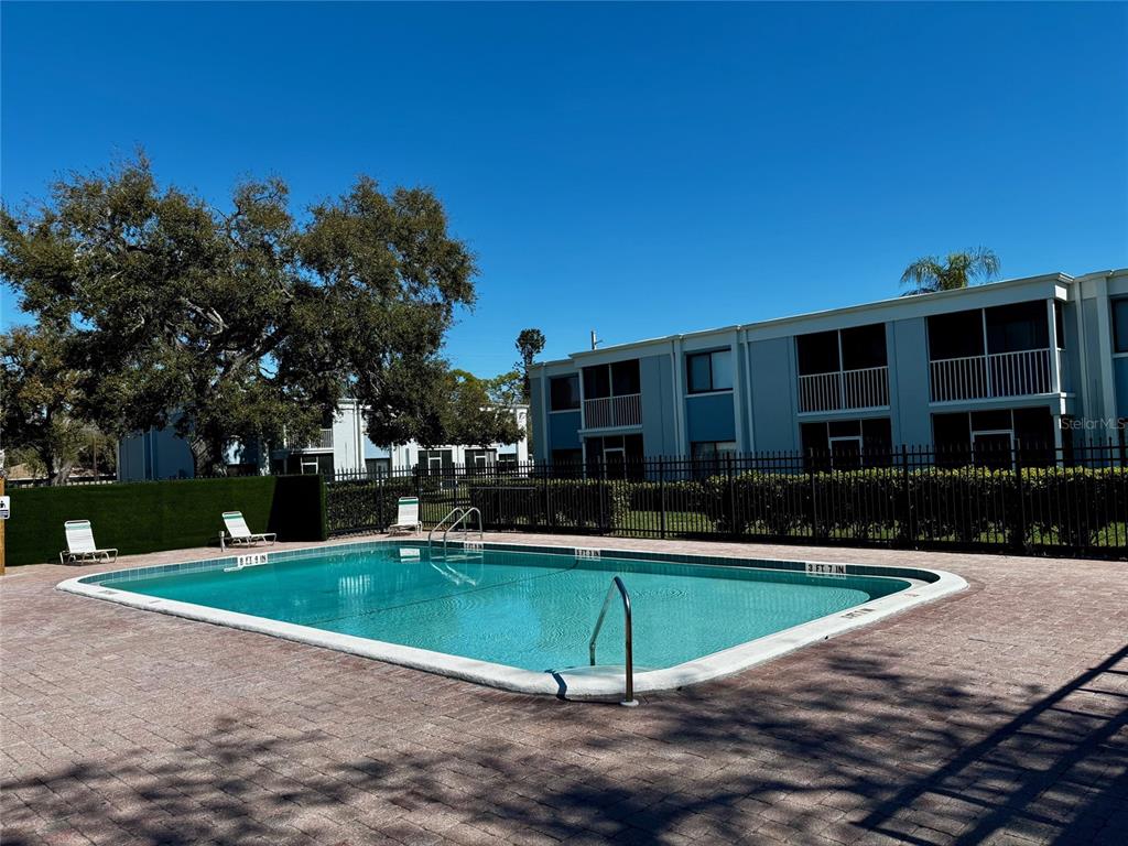 A rectangular swimming pool sits on a brick patio in front of a multi-story apartment building — 5310 26TH STREET W UNIT 902, BRADENTON, FL