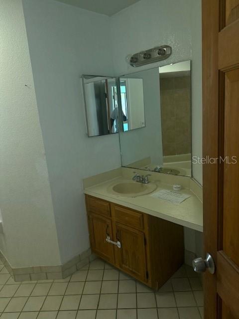 A bathroom features a wooden vanity with a sink, a mirror, and tiled flooring — 3620 SAWGRASS DRIVE, TITUSVILLE, FL