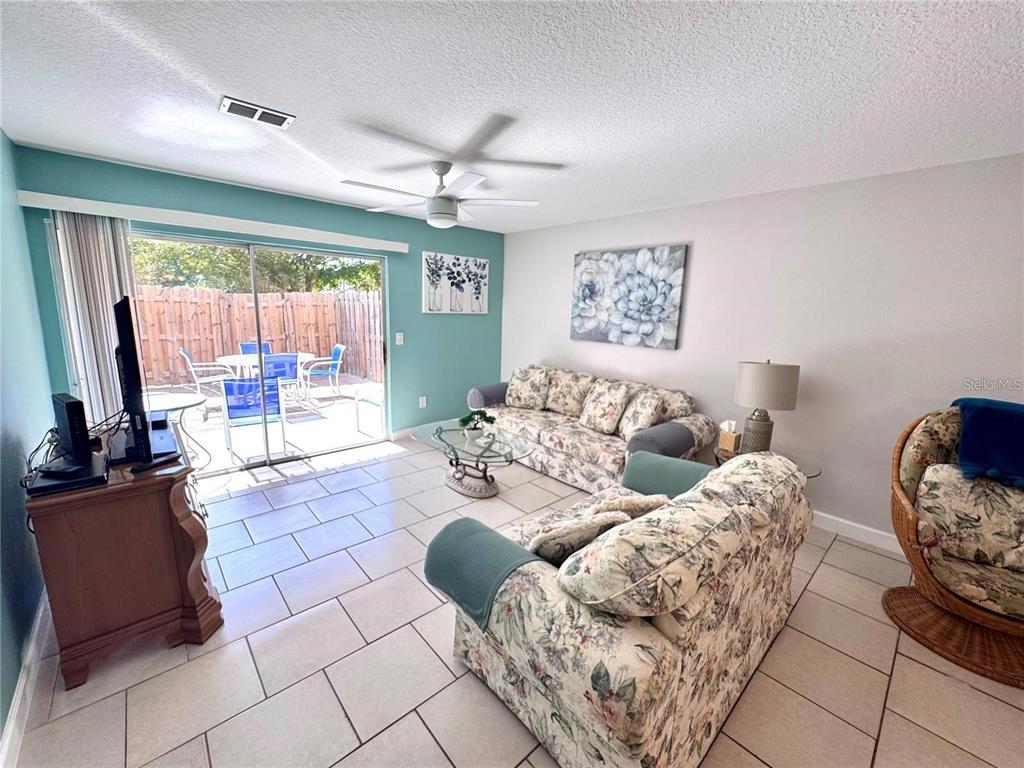 A living room features floral sofas, tile flooring, a ceiling fan, and a sliding glass door — 3473 CLARK ROAD UNIT 171, SARASOTA, FL