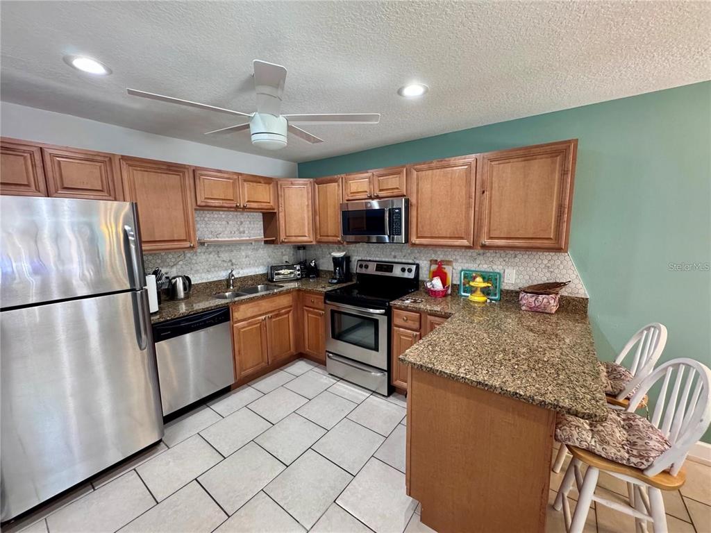A kitchen features wood cabinets, granite countertops, stainless steel appliances, and a tiled floor — 3473 CLARK ROAD UNIT 171, SARASOTA, FL