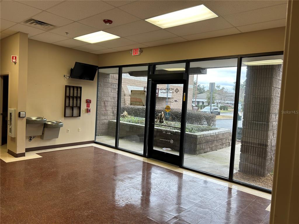 An empty commercial lobby features brown tile flooring, a water fountain, and glass entrance doors — 3300 SW 34TH AVENUE UNIT 104 & 108, OCALA, FL