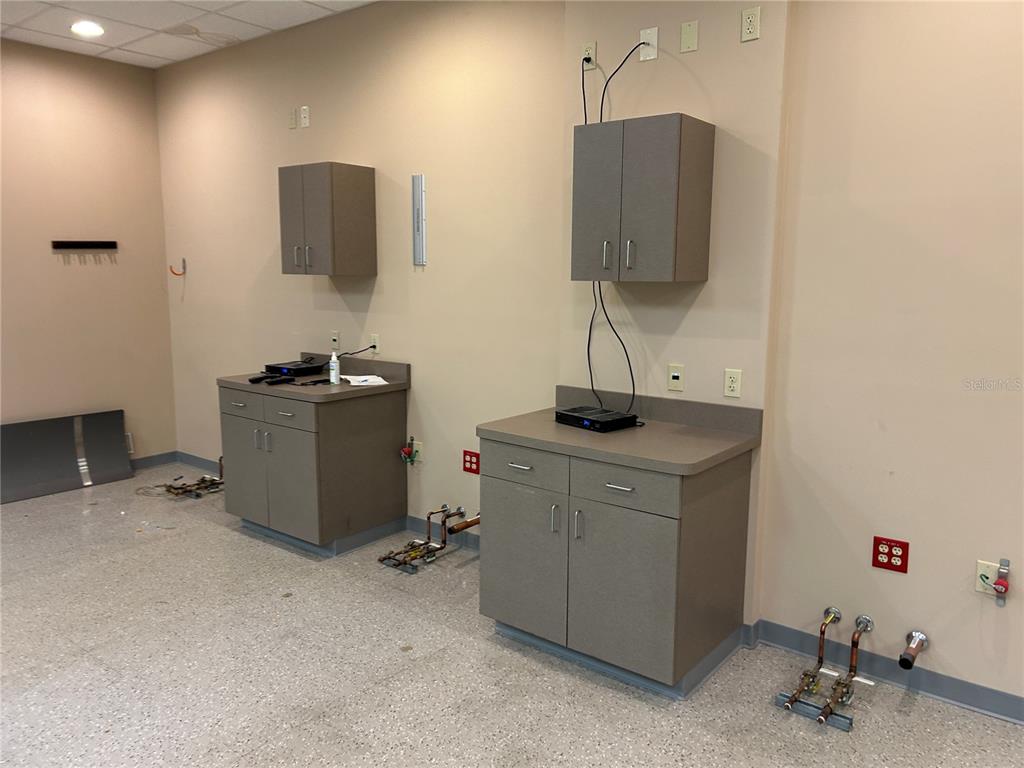 A commercial room features two sets of grey cabinets, exposed plumbing, and beige walls — 3300 SW 34TH AVENUE UNIT 104 & 108, OCALA, FL