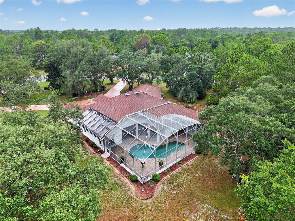 An aerial view shows a house with a screened-in pool and a large wooded yard — 2155 W FIR PLACE, BEVERLY HILLS, FL