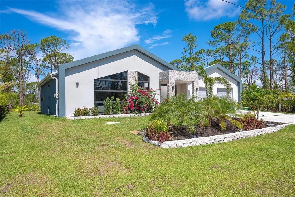 A modern single-story house with a stone-accented entryway and large windows sits on a lawn — 8167 DITTMAR STREET, PORT CHARLOTTE, FL