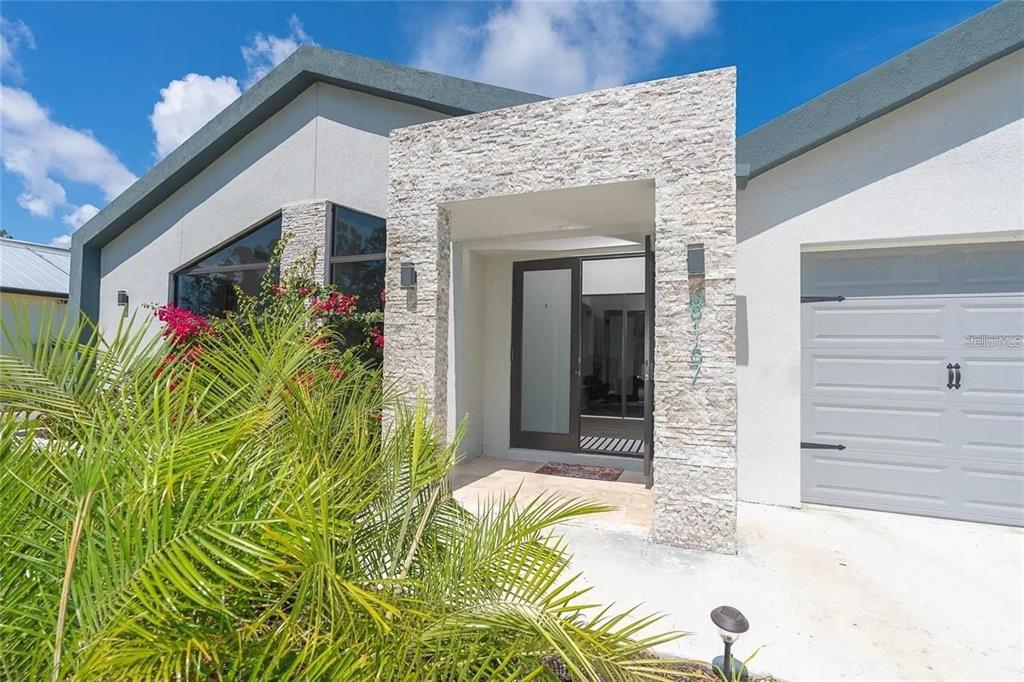 The exterior of a modern house features a stone-clad entryway and a gray garage door — 8167 DITTMAR STREET, PORT CHARLOTTE, FL