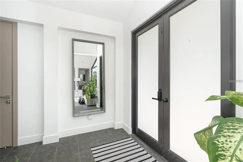 A modern entryway features a large wall mirror, dark tile flooring, and black-framed glass doors — 8167 DITTMAR STREET, PORT CHARLOTTE, FL