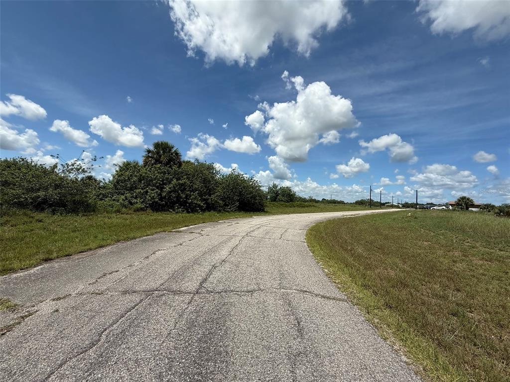 A paved road curves through a grassy, undeveloped lot under a bright, cloudy sky — 113 LIBERTY TERRACE, LABELLE, FL