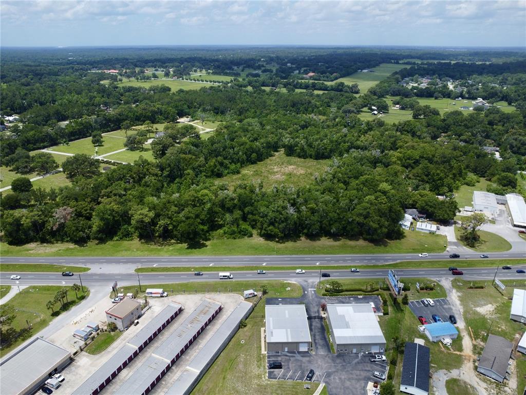An aerial view shows a wooded lot situated across a highway from commercial buildings — TBD S PINE AVENUE, OCALA, FL