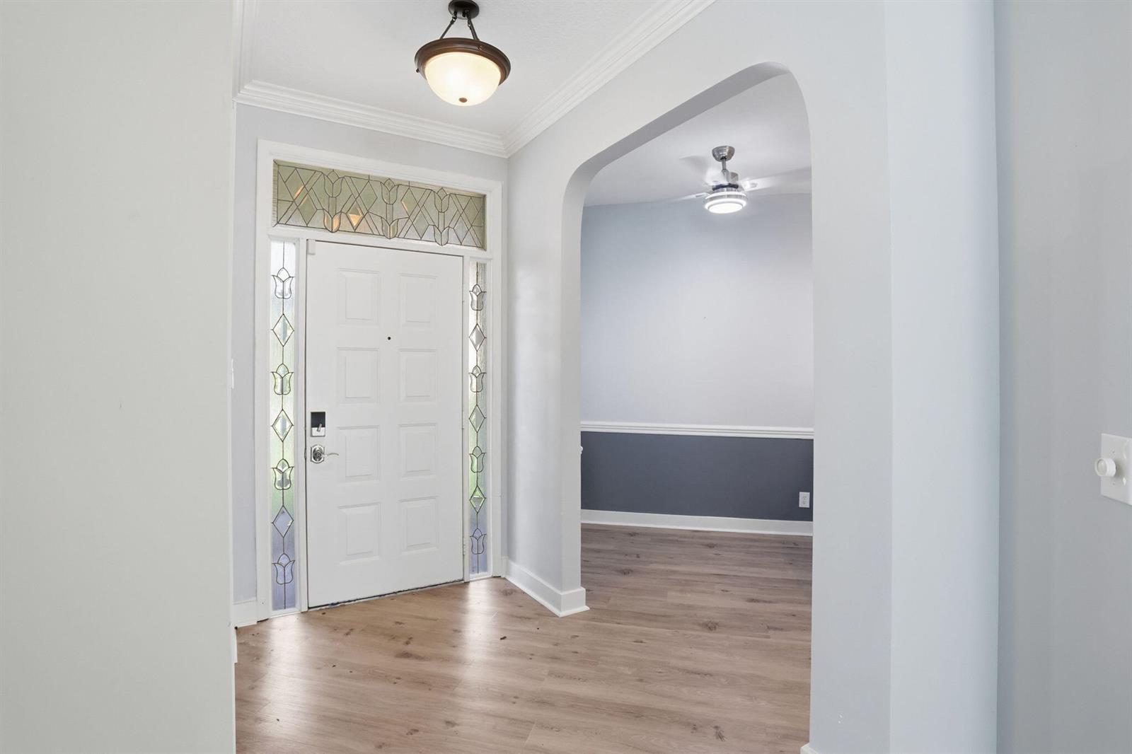 An entryway with light wood flooring, a white front door, and an arched doorway — 7725 Mansfield Hollow Road, Delray Beach FL 33446, DELRAY BEACH, FL