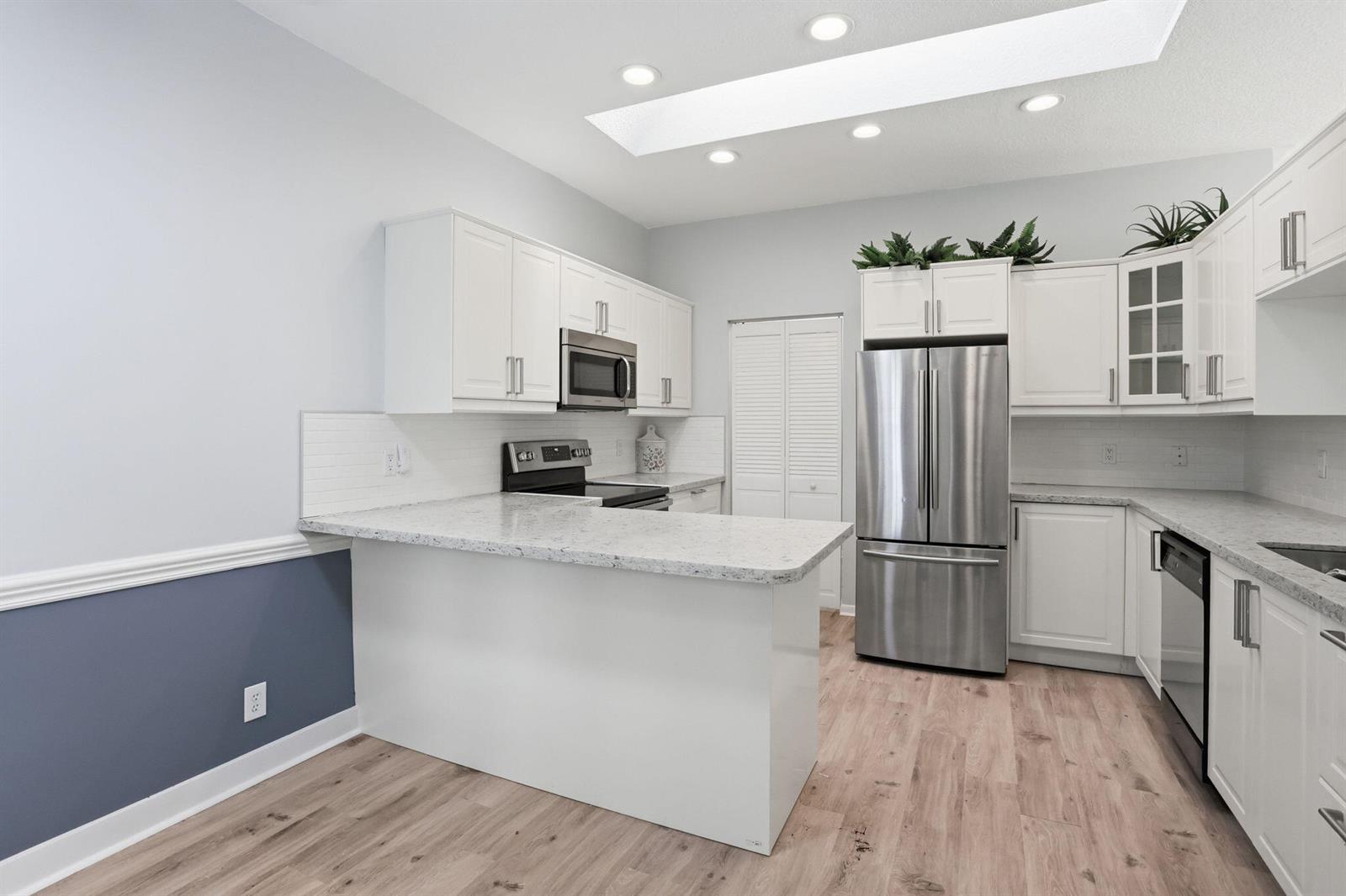 A kitchen features white cabinets, granite countertops, stainless steel appliances, and light wood-look flooring — 7725 Mansfield Hollow Road, Delray Beach FL 33446, DELRAY BEACH, FL