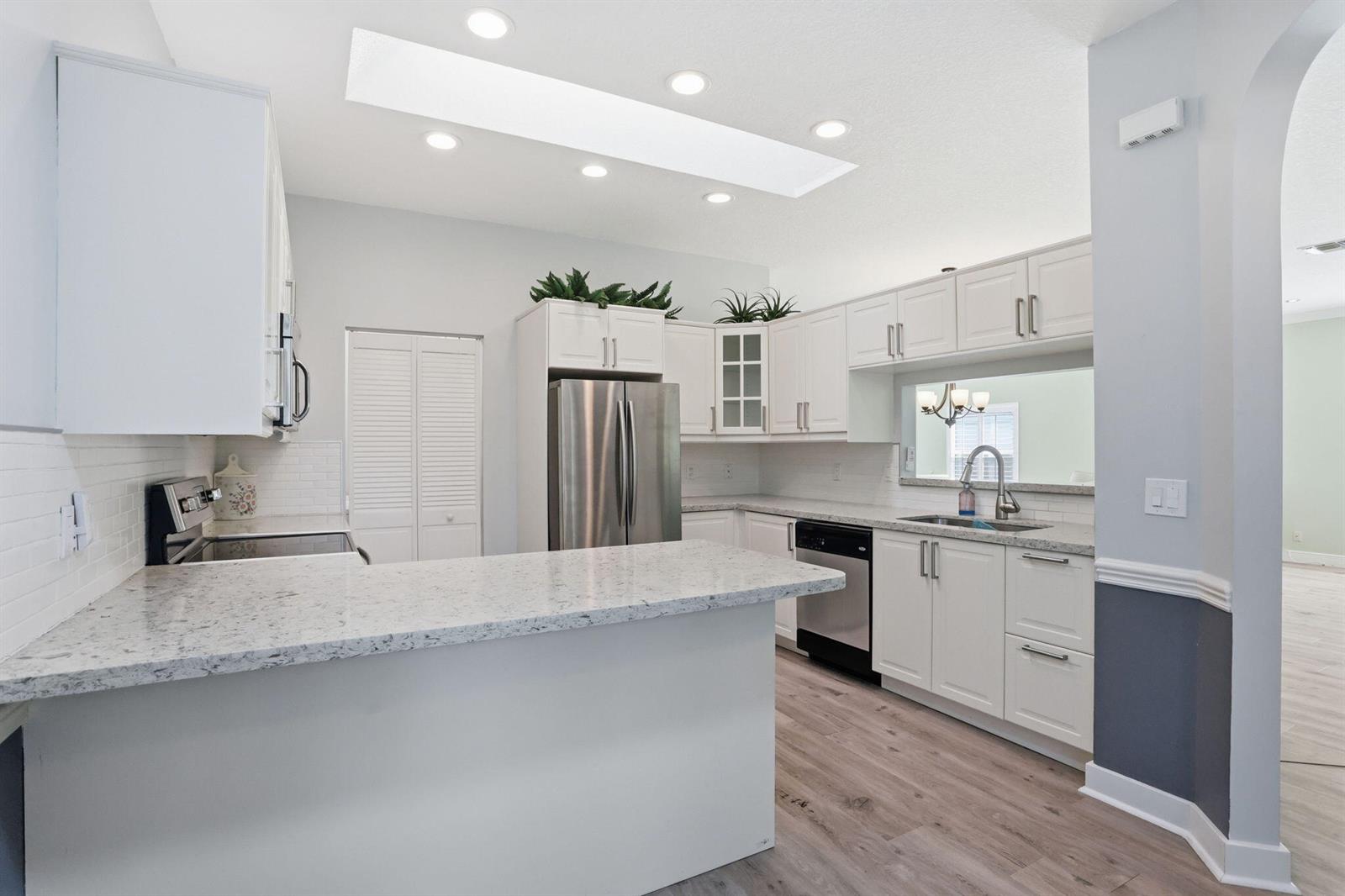 A kitchen features white cabinets, granite countertops, stainless steel appliances, and light wood flooring — 7725 Mansfield Hollow Road, Delray Beach FL 33446, DELRAY BEACH, FL