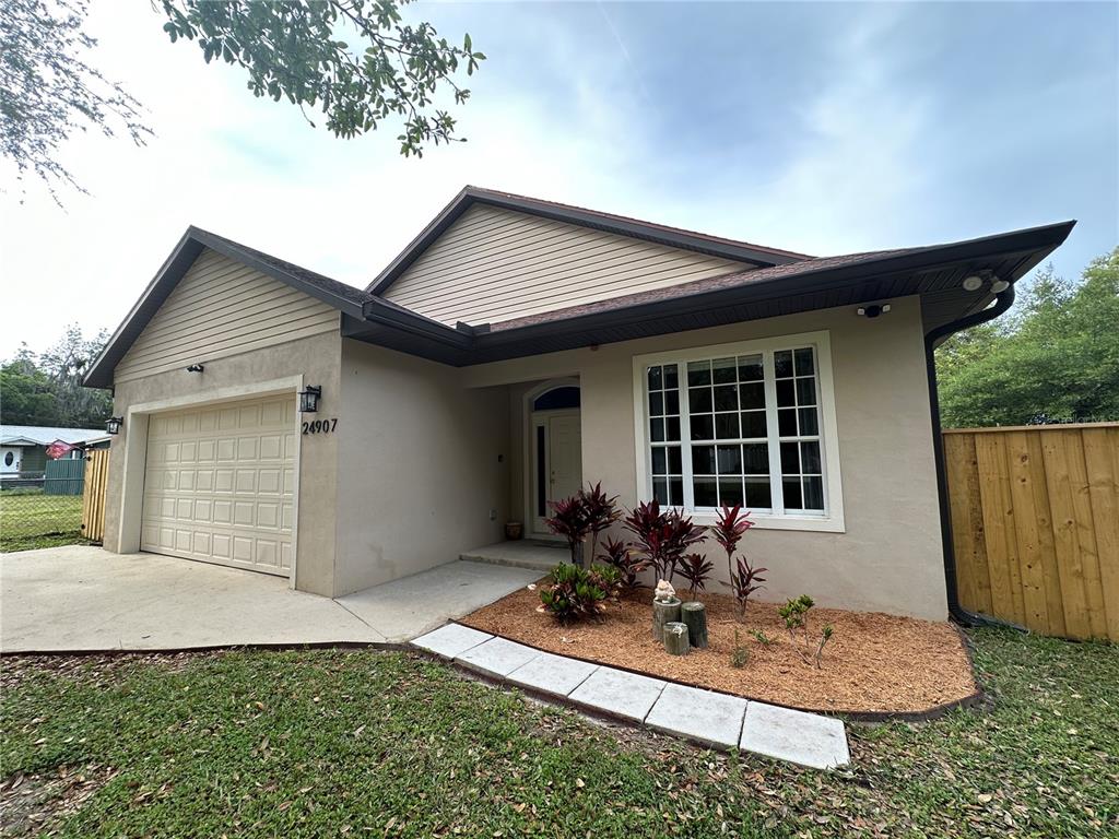 A single-story house with a beige stucco exterior, a garage, and a front garden bed — 24907 NE 135TH STREET, SALT SPRINGS, FL