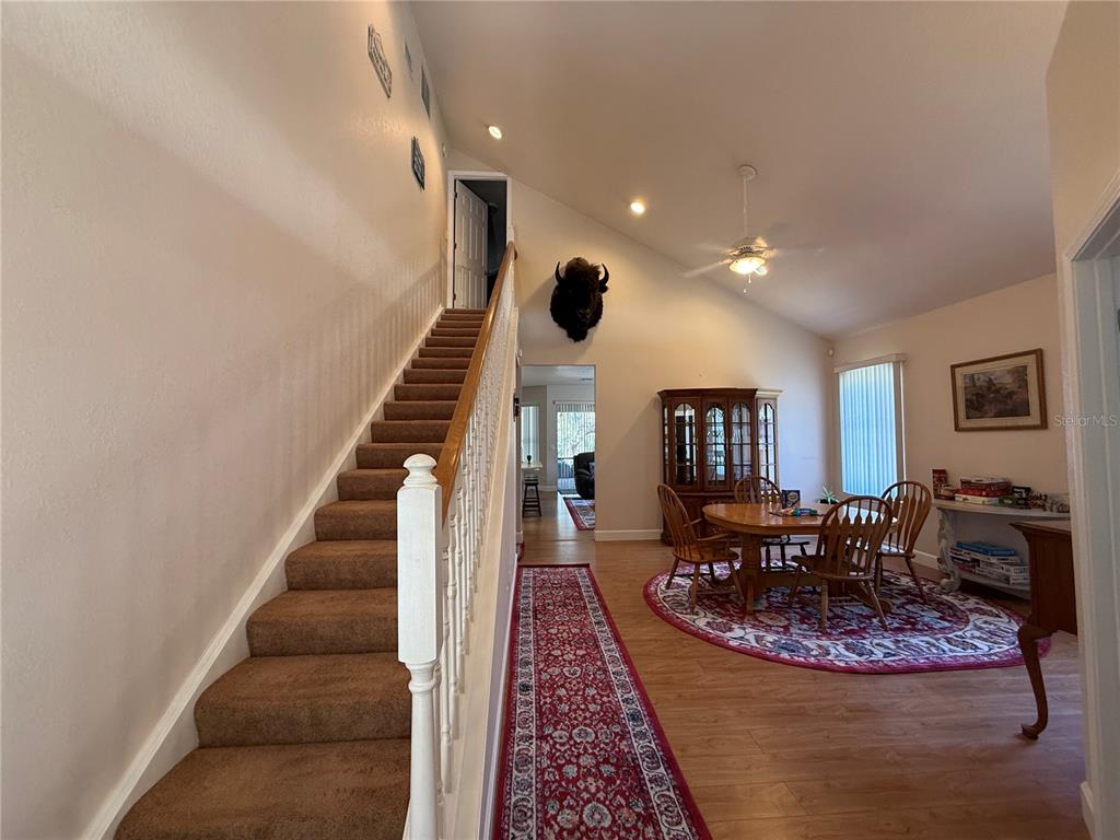 A carpeted staircase leads to an upper level next to a dining area with wood flooring — 24907 NE 135TH STREET, SALT SPRINGS, FL