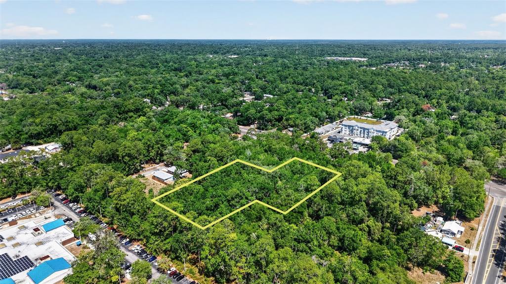 An aerial view shows a wooded lot outlined in yellow surrounded by commercial and residential buildings — TBD SE 2ND AVENUE, GAINESVILLE, FL