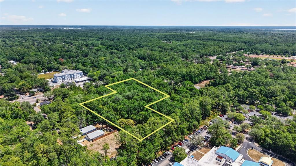 An aerial view shows a wooded lot outlined in yellow near commercial buildings and roads — TBD SE 2ND AVENUE, GAINESVILLE, FL