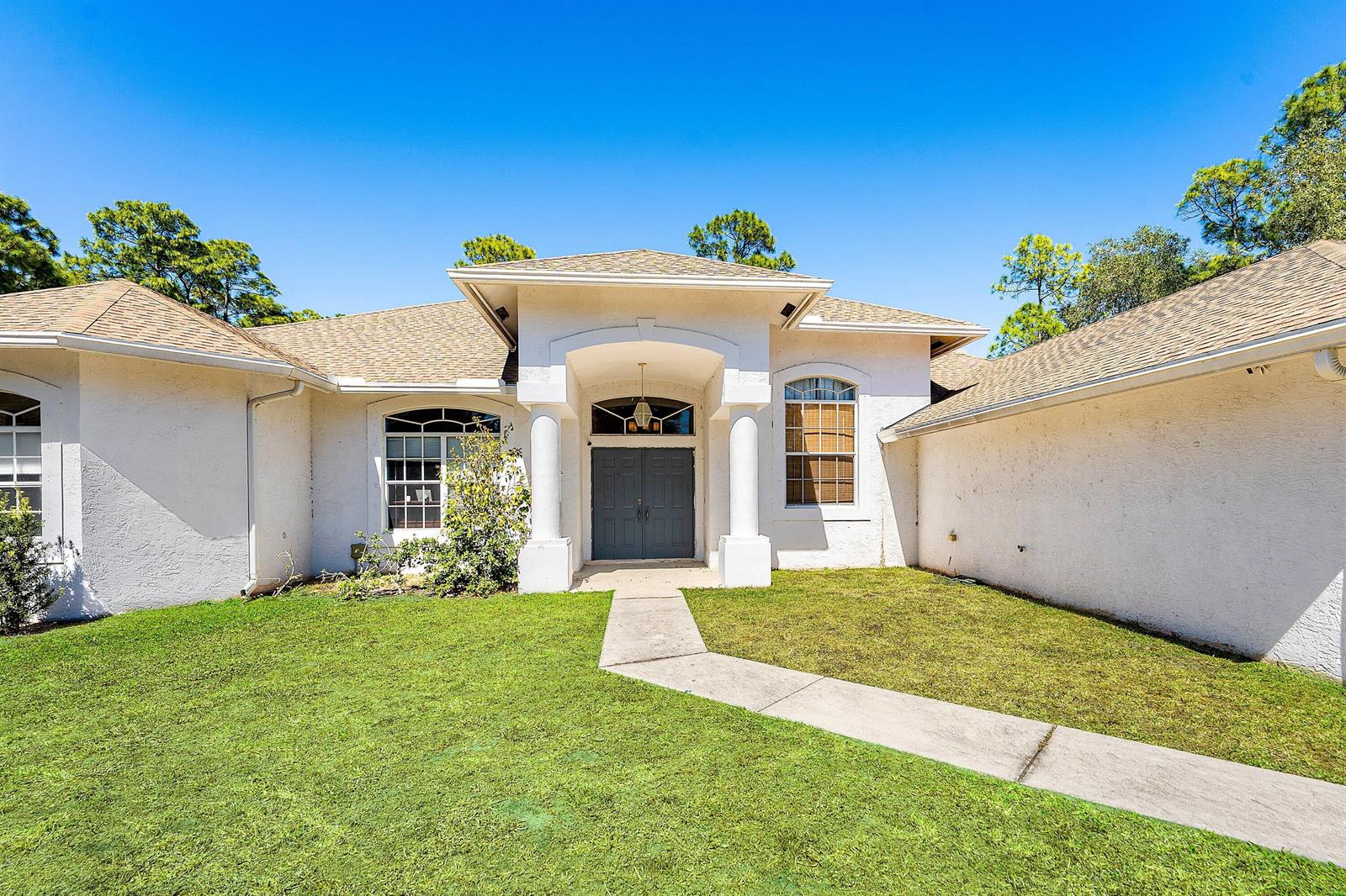 A single-story house with a white stucco facade, double front doors, and a concrete walkway — 17225 80th Street N, FL 33470, FL