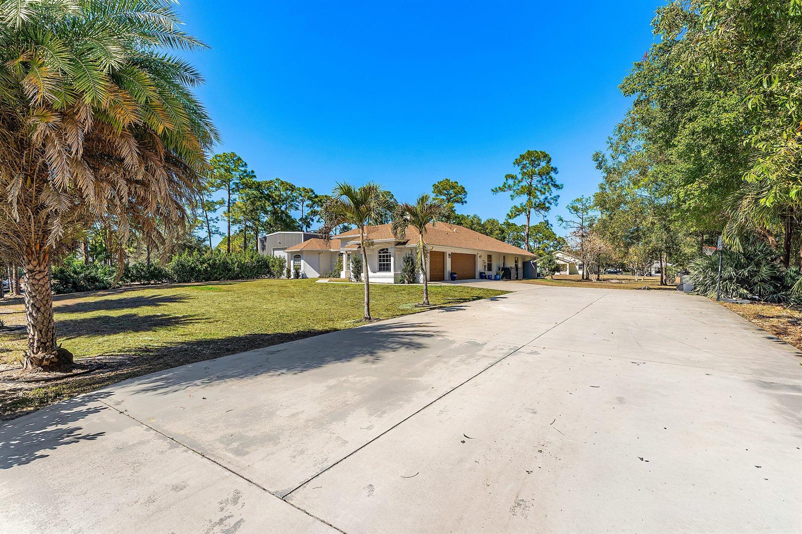 A wide concrete driveway leads to a single-story house with a multi-car garage and palms — 17225 80th Street N, FL 33470, FL