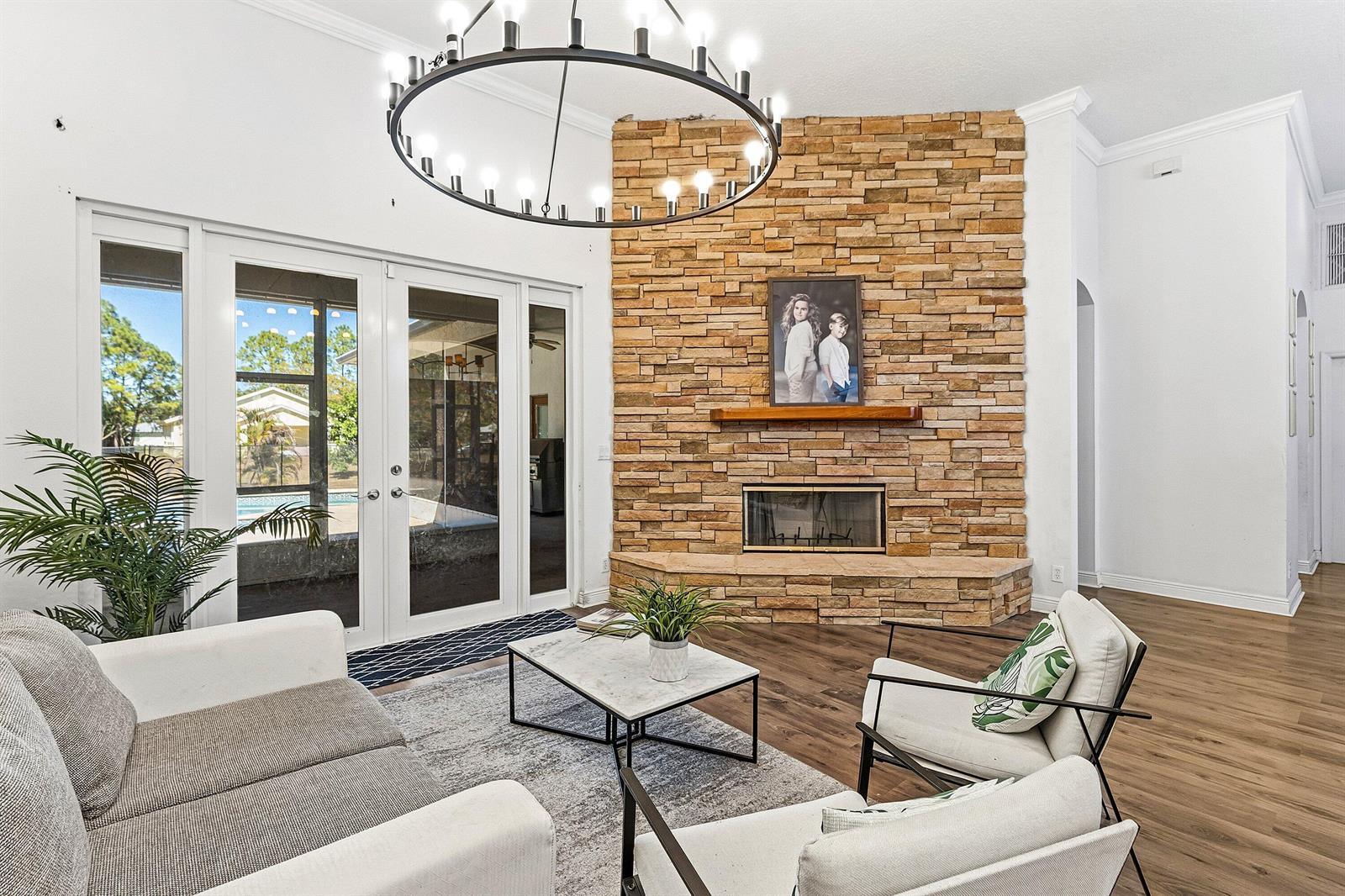 A living room features a stone fireplace, a large chandelier, and glass doors to a patio — 17225 80th Street N, FL 33470, FL