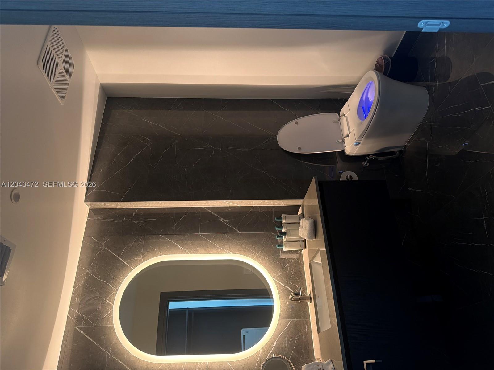 A modern bathroom features dark marble tile, a backlit oval mirror, and a smart toilet — 20 NE 11th St # 2409, Miami FL 33132, MIAMI, FL
