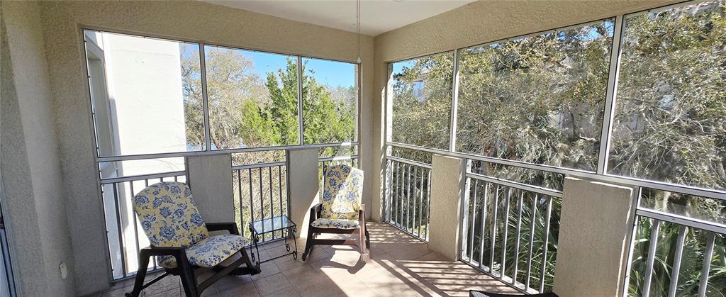 A screened-in porch features tiled flooring, two rocking chairs, and views of surrounding trees — 45 RIVERVIEW BEND S UNIT 1937, PALM COAST, FL