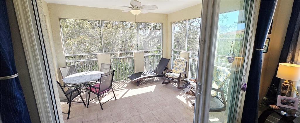 A screened-in balcony features tiled flooring, a ceiling fan, and outdoor furniture overlooking trees — 45 RIVERVIEW BEND S UNIT 1937, PALM COAST, FL