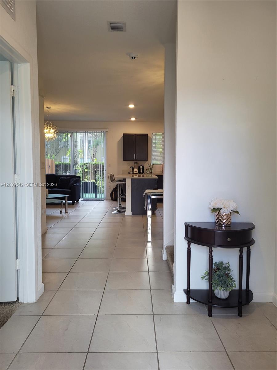 A tiled hallway leads to an open-concept living area with a kitchen and sliding glass doors — 1015 SE 24th Ter, Homestead FL 33035, HOMESTEAD, FL