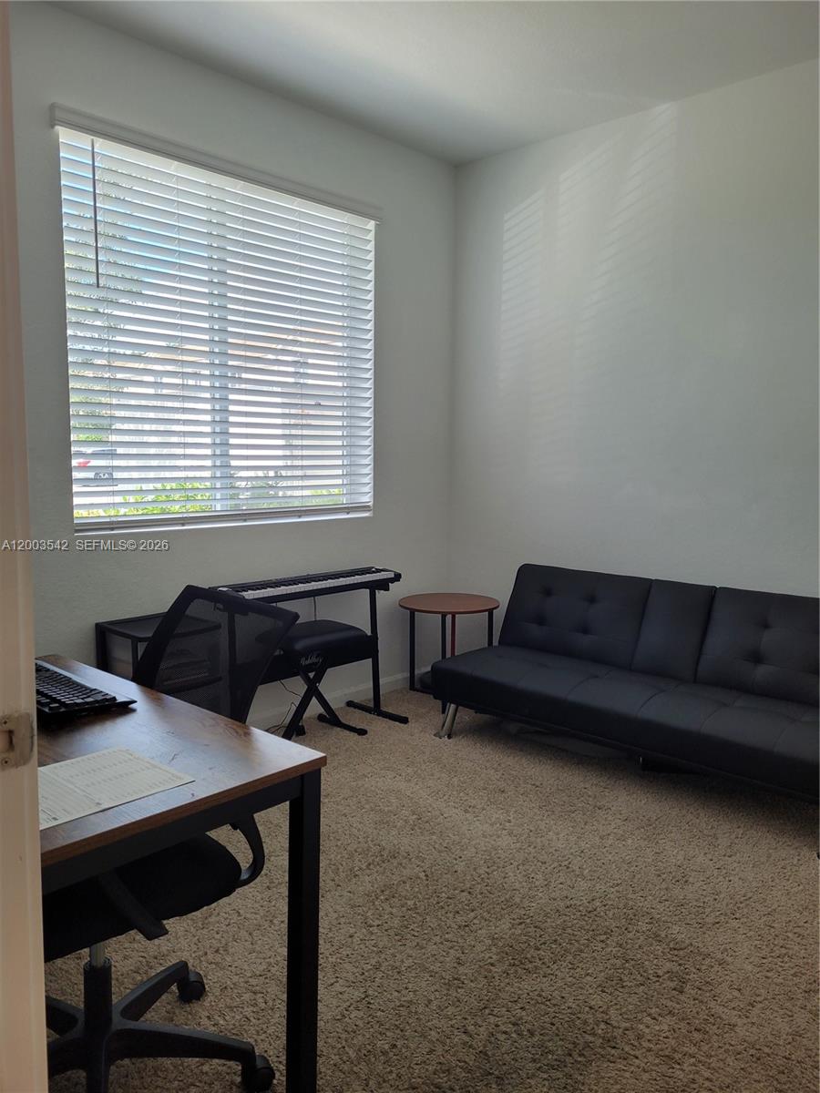 A room with carpeted flooring, a desk, a keyboard, and a black futon sofa — 1015 SE 24th Ter, Homestead FL 33035, HOMESTEAD, FL