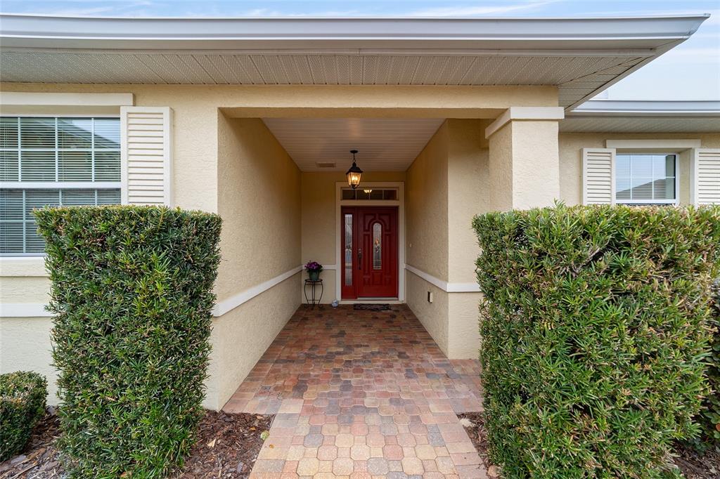 A paved walkway leads to a covered entryway with a red front door and hedges — 8835 SW 83RD COURT ROAD, OCALA, FL