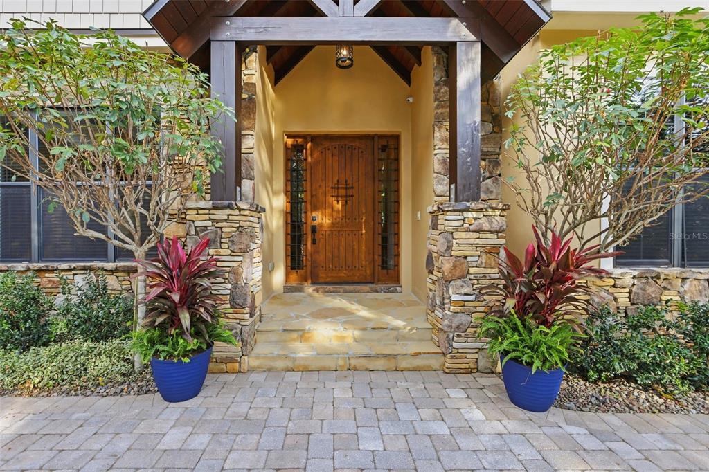 A stone-accented entryway features a wooden front door, a covered porch, and two potted plants — 713 MAIN STREET, WINDERMERE, FL