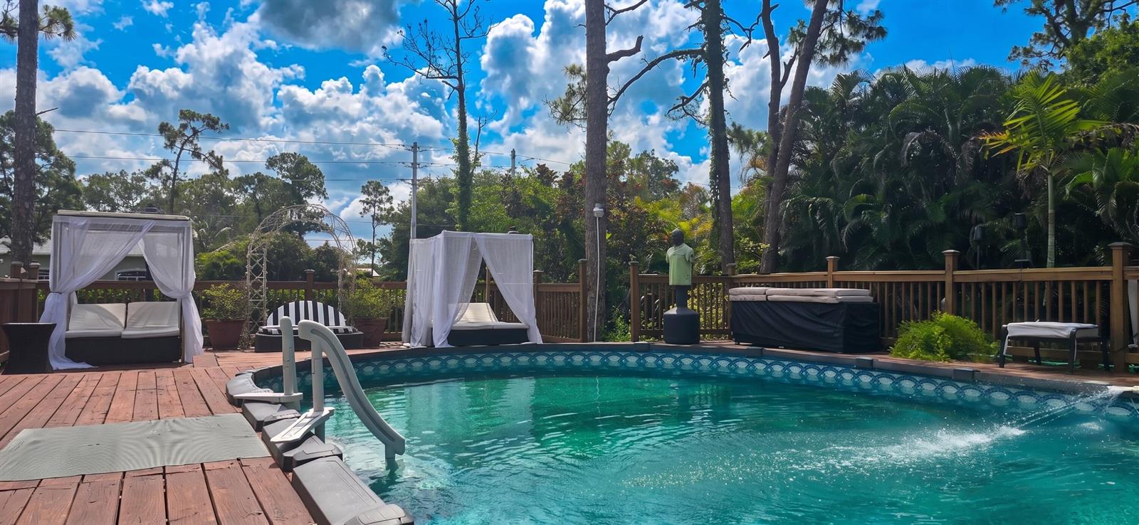 A backyard swimming pool features a wooden deck, two white canopy daybeds, and lush landscaping — 15056 Temple Boulevard, FL 33470, FL