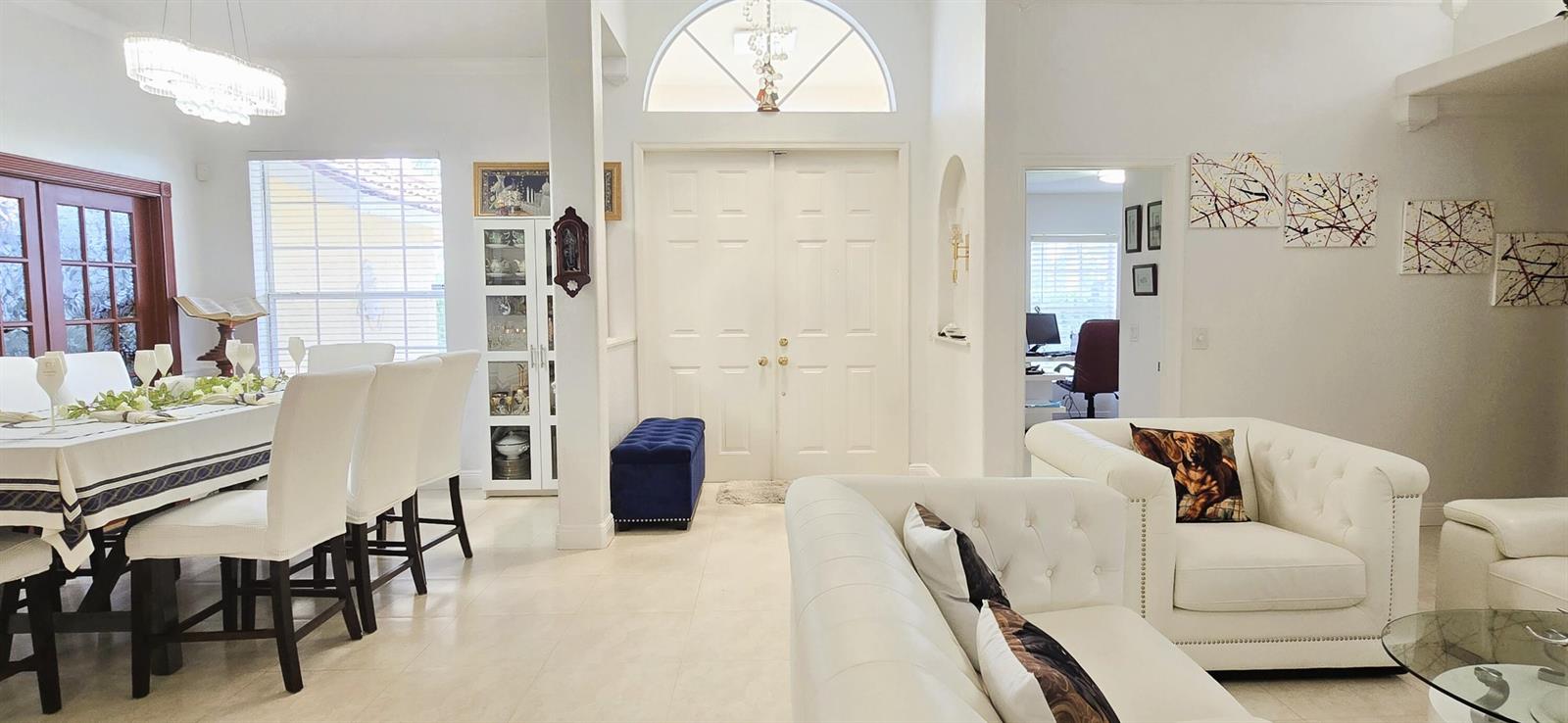 A bright, open-concept living and dining area features white tufted furniture, tile flooring, and double entry doors — 15056 Temple Boulevard, FL 33470, FL