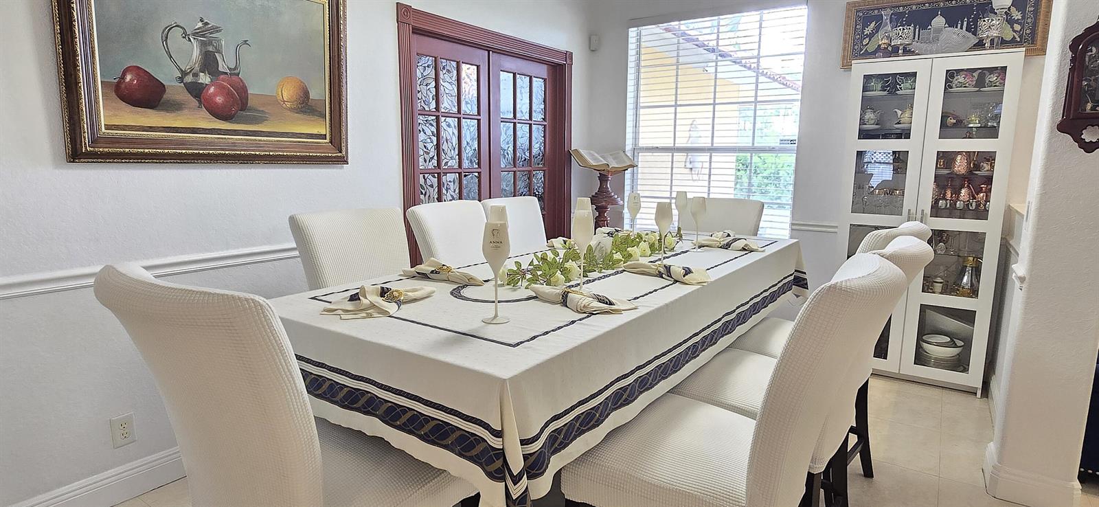 A dining room features a long table set for dinner, white chairs, and a display cabinet — 15056 Temple Boulevard, FL 33470, FL