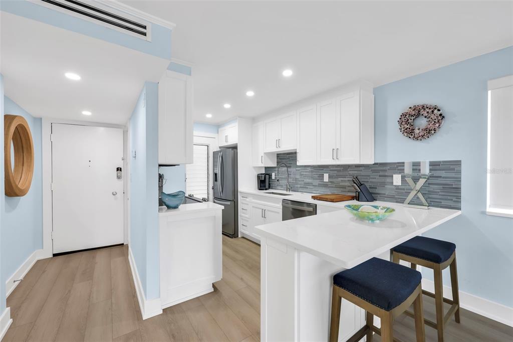 A kitchen features white cabinets, a quartz breakfast bar, and blue-gray tile backsplash — 1300 GULF SHORE BOULEVARD N UNIT 700, NAPLES, FL