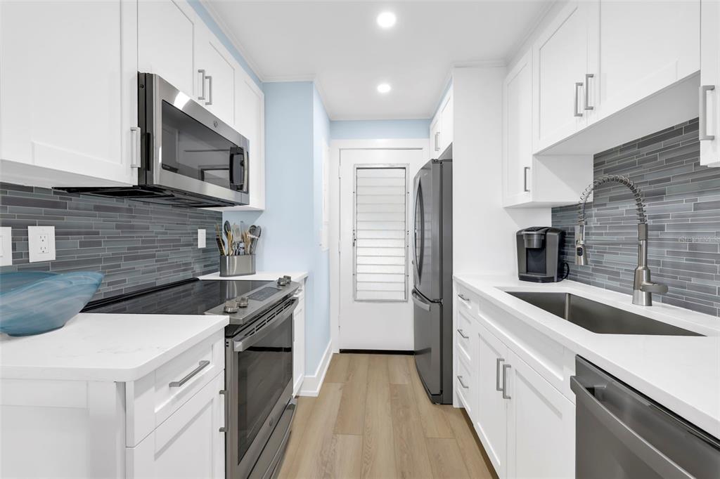 A galley kitchen features white cabinets, stainless steel appliances, and a gray tiled backsplash — 1300 GULF SHORE BOULEVARD N UNIT 700, NAPLES, FL