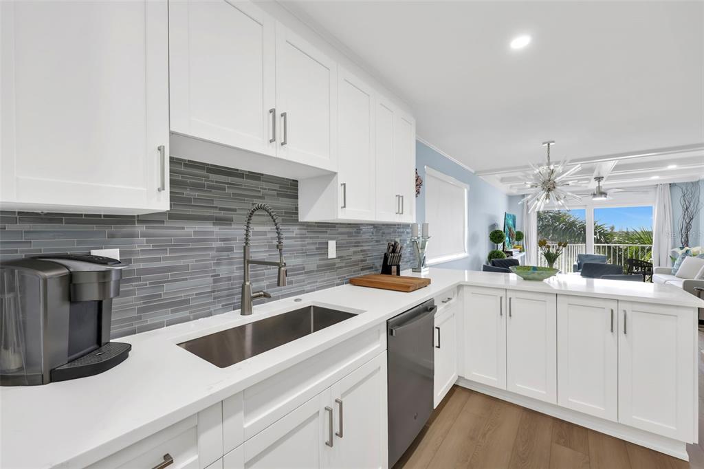 A white kitchen features gray tile backsplash, stainless steel appliances, and a view of the living area — 1300 GULF SHORE BOULEVARD N UNIT 700, NAPLES, FL