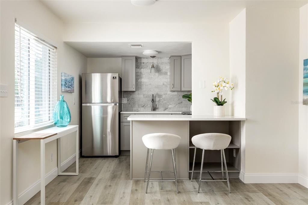 A kitchen features gray cabinets, a stainless steel refrigerator, and a breakfast bar with stools — 1142 SUNSET POINT ROAD, CLEARWATER, FL
