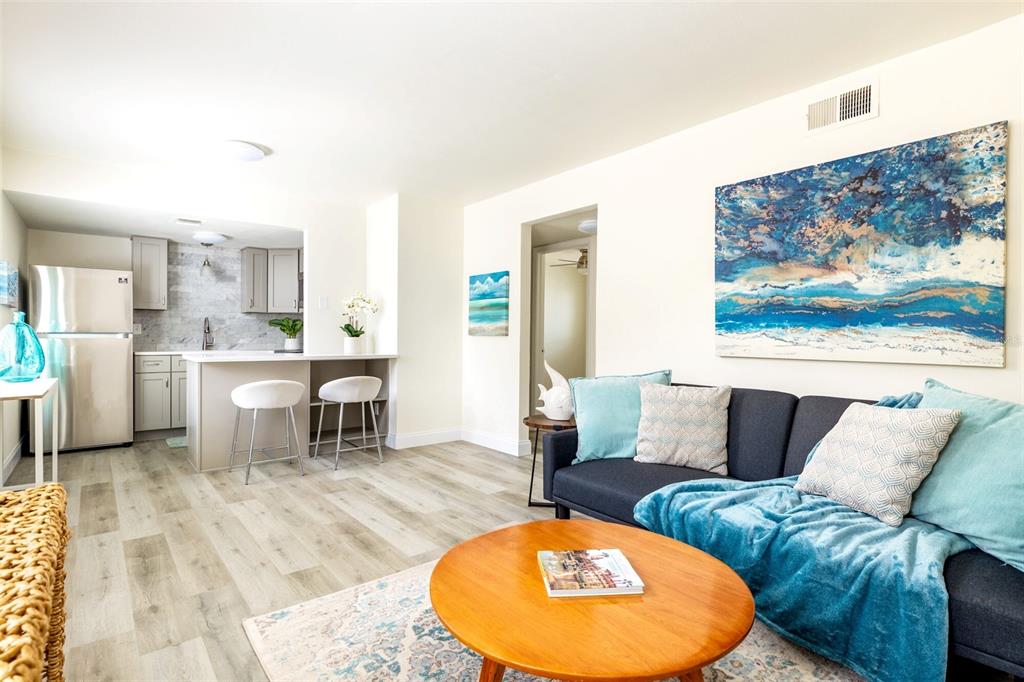 A living room with light wood flooring, a dark sofa, and an open kitchen area — 1142 SUNSET POINT ROAD, CLEARWATER, FL