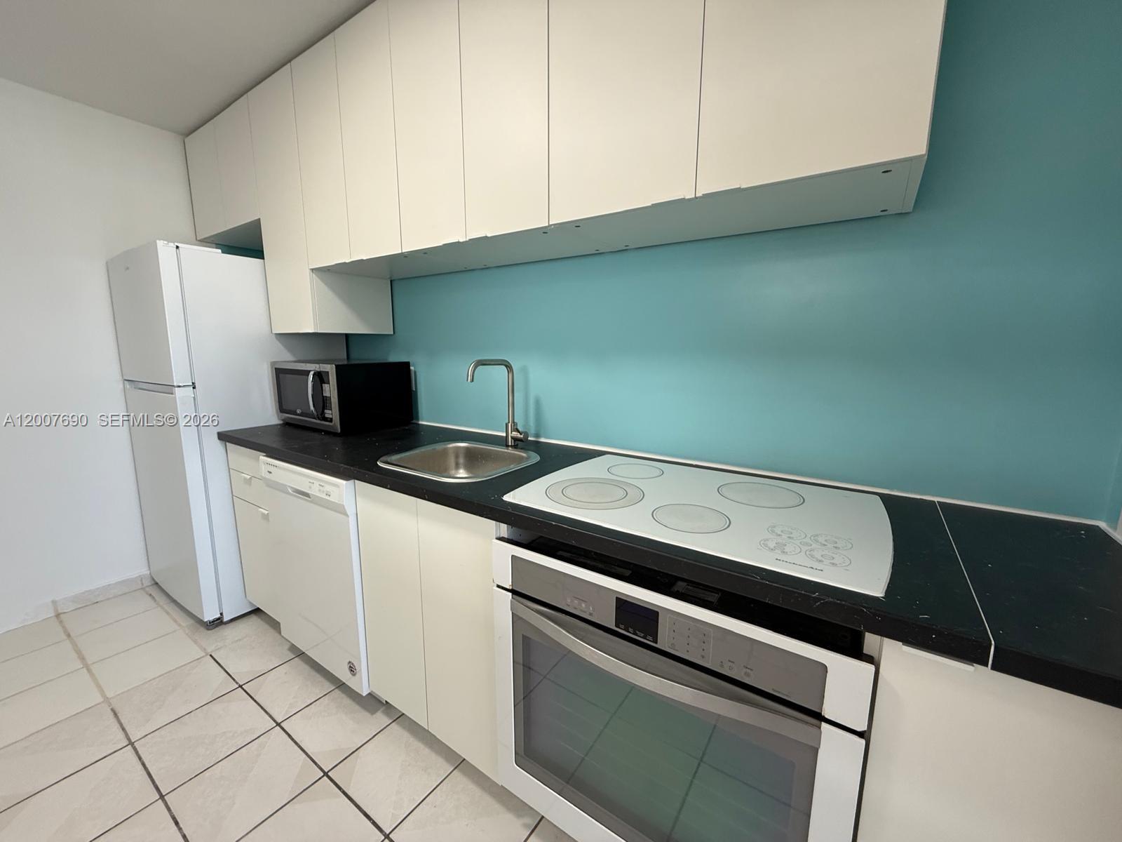 A kitchen features white cabinets, a black countertop, a teal backsplash, and white appliances — 1750 James Ave # 7A, Miami Beach FL 33139, MIAMI BEACH, FL