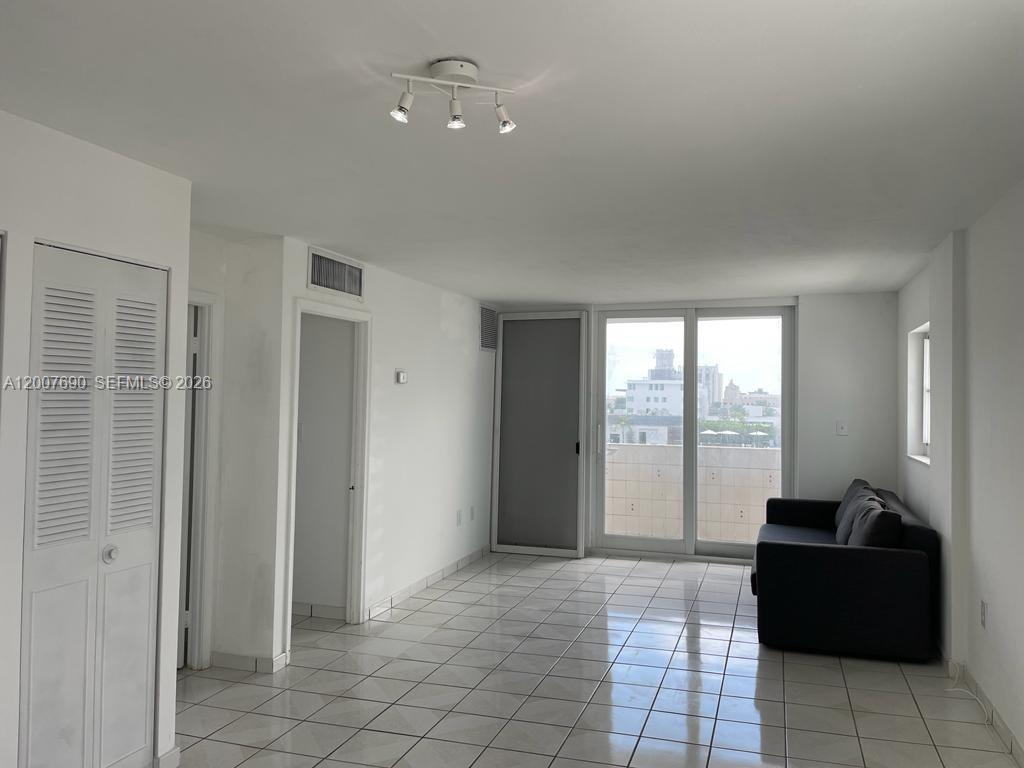 A bright living room features white tile floors, a dark sofa, and a sliding glass door — 1750 James Ave # 7A, Miami Beach FL 33139, MIAMI BEACH, FL