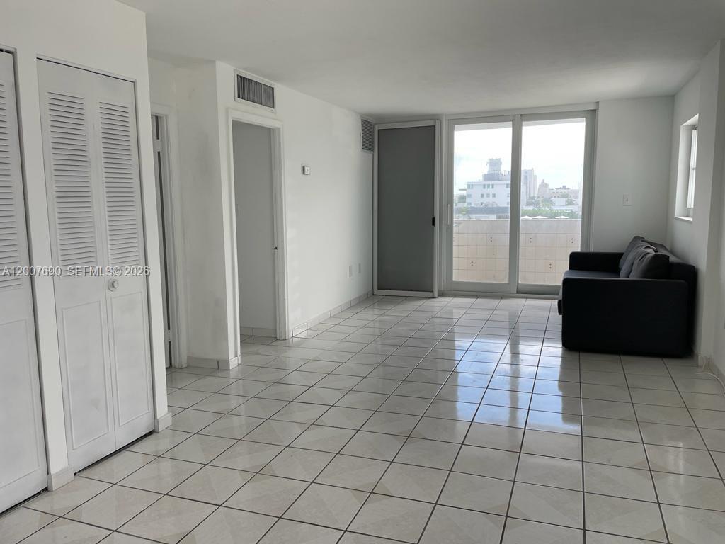 A bright living room features white walls, white tile flooring, a dark sofa, and sliding doors — 1750 James Ave # 7A, Miami Beach FL 33139, MIAMI BEACH, FL