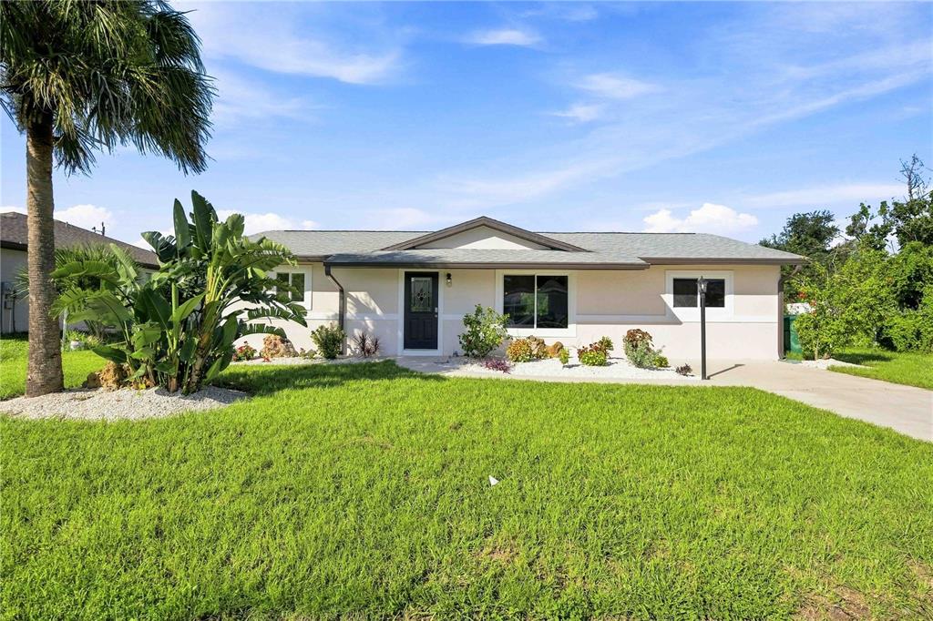 A single-story house with a light-colored exterior, a dark front door, and a palm tree — 7321 BOLTEN LANE, PORT CHARLOTTE, FL