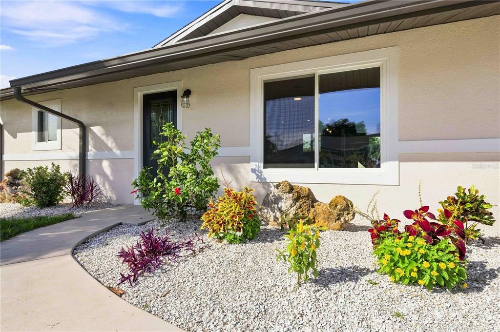 The exterior of a house features a light-colored facade, a dark front door, and landscaping — 7321 BOLTEN LANE, PORT CHARLOTTE, FL