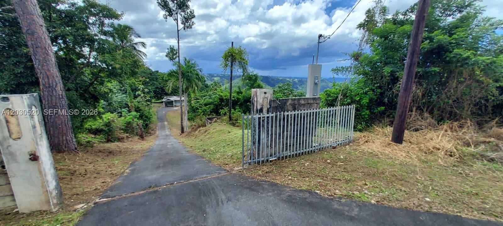 A paved driveway leads down a grassy slope toward a distant house and mountain view — #22, Bo Vaga vaga, PR 00687, PR