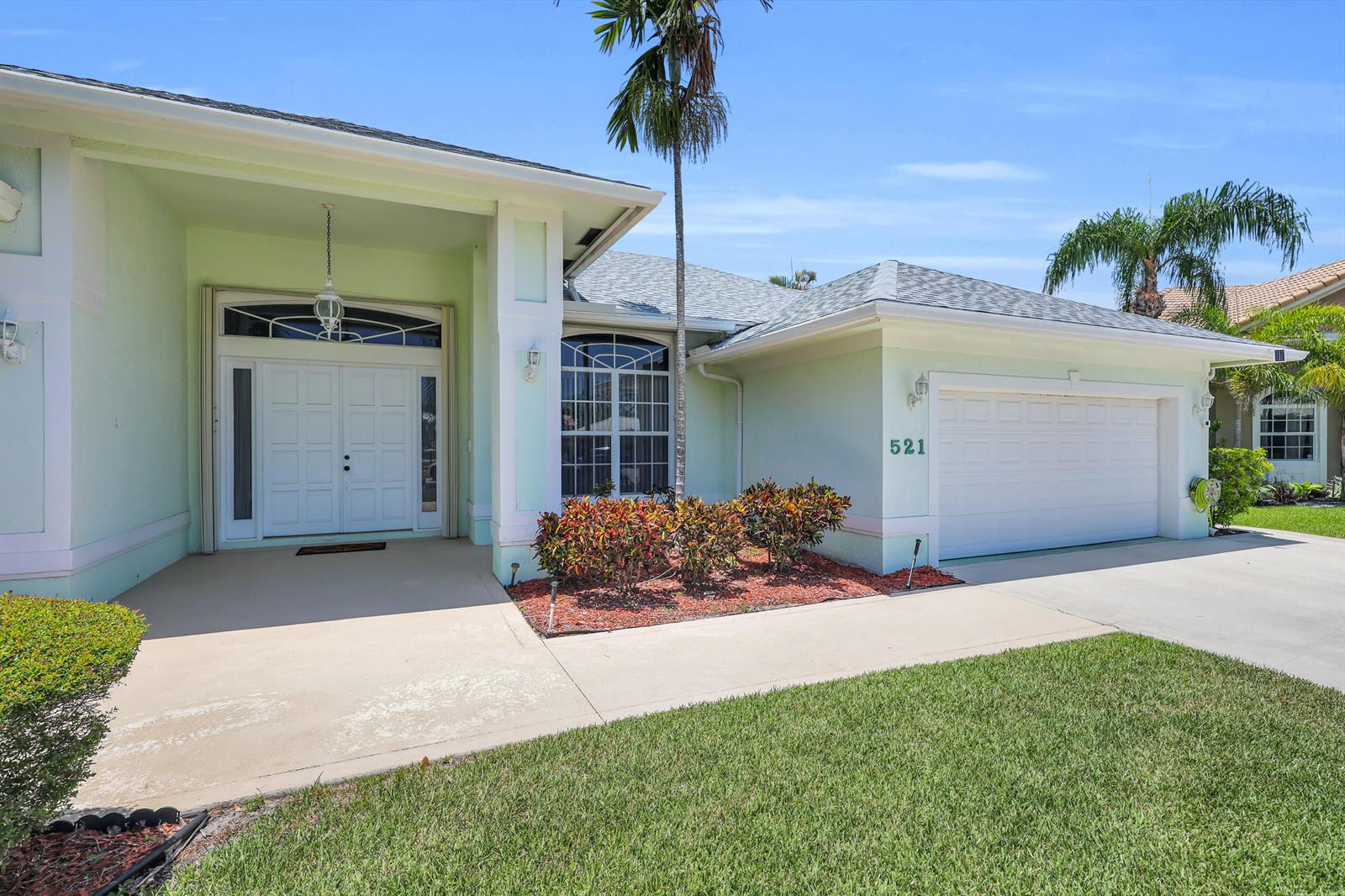 A light green house features a double front door, a garage, and a palm tree — 521 Cypress Circle, Tequesta FL 33469, TEQUESTA, FL